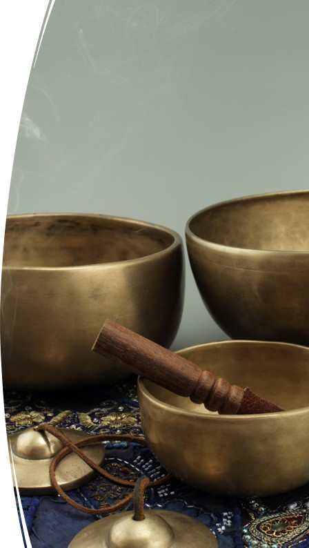 Bronze singing bowls and mallet on patterned cloth, with small bell and incense holder nearby.